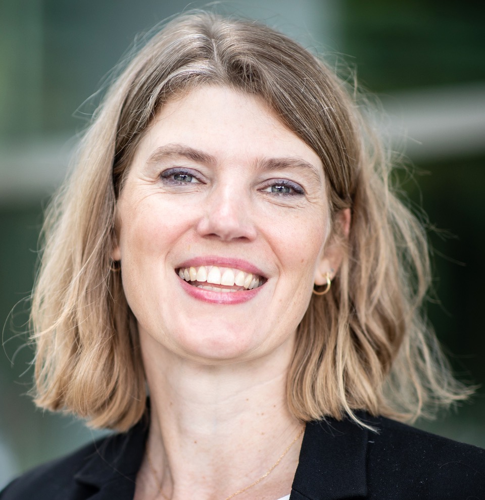 Portret van Astrid Hendriks met een glimlach, genomen in een buitenomgeving.