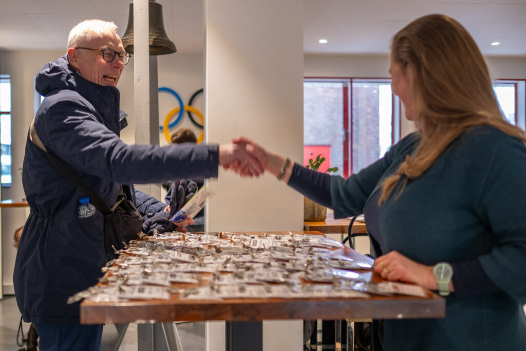 Een man en een vrouw schudden elkaar de hand bij een ontvangsttafel vol naamkaartjes tijdens een Breikers-evenement.