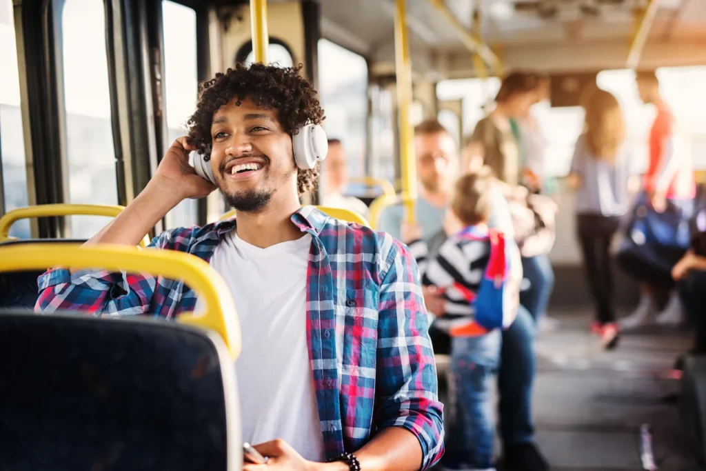 Man met koptelefoon voert een telefoongesprek en lacht terwijl hij in een bus zit.