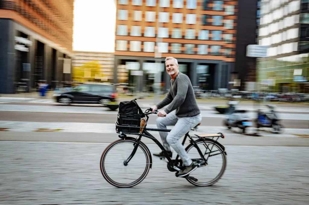 Man fietst glimlachend door een moderne stad met een rugtas in een krat op het voorrek.