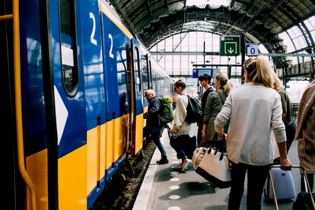 Reizigers stappen in een gele en blauwe trein op station Breikers onder een overdekt perron.