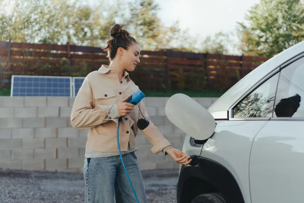 Vrouw sluit een elektrische auto aan op een laadkabel bij een laadpunt.