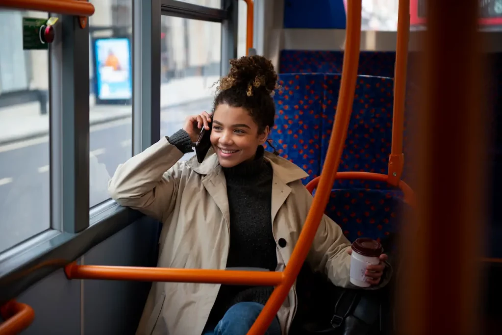 Jonge vrouw voert een telefoongesprek en houdt een koffiebeker vast terwijl ze in de bus zit.