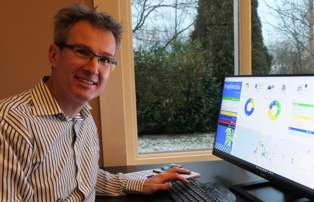 Man in gestreept overhemd werkt achter een computerscherm met mobiliteitsdata in een kantoor met uitzicht op een tuin.