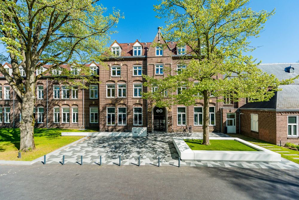 Het historische EO-gebouw in Hilversum met rode bakstenen gevel en omliggende bomen op een zonnige dag.