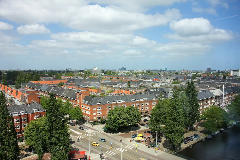 Luchtfoto van een woonwijk met karakteristieke bakstenen gebouwen en grachten in Amsterdam onder een deels bewolkte hemel.