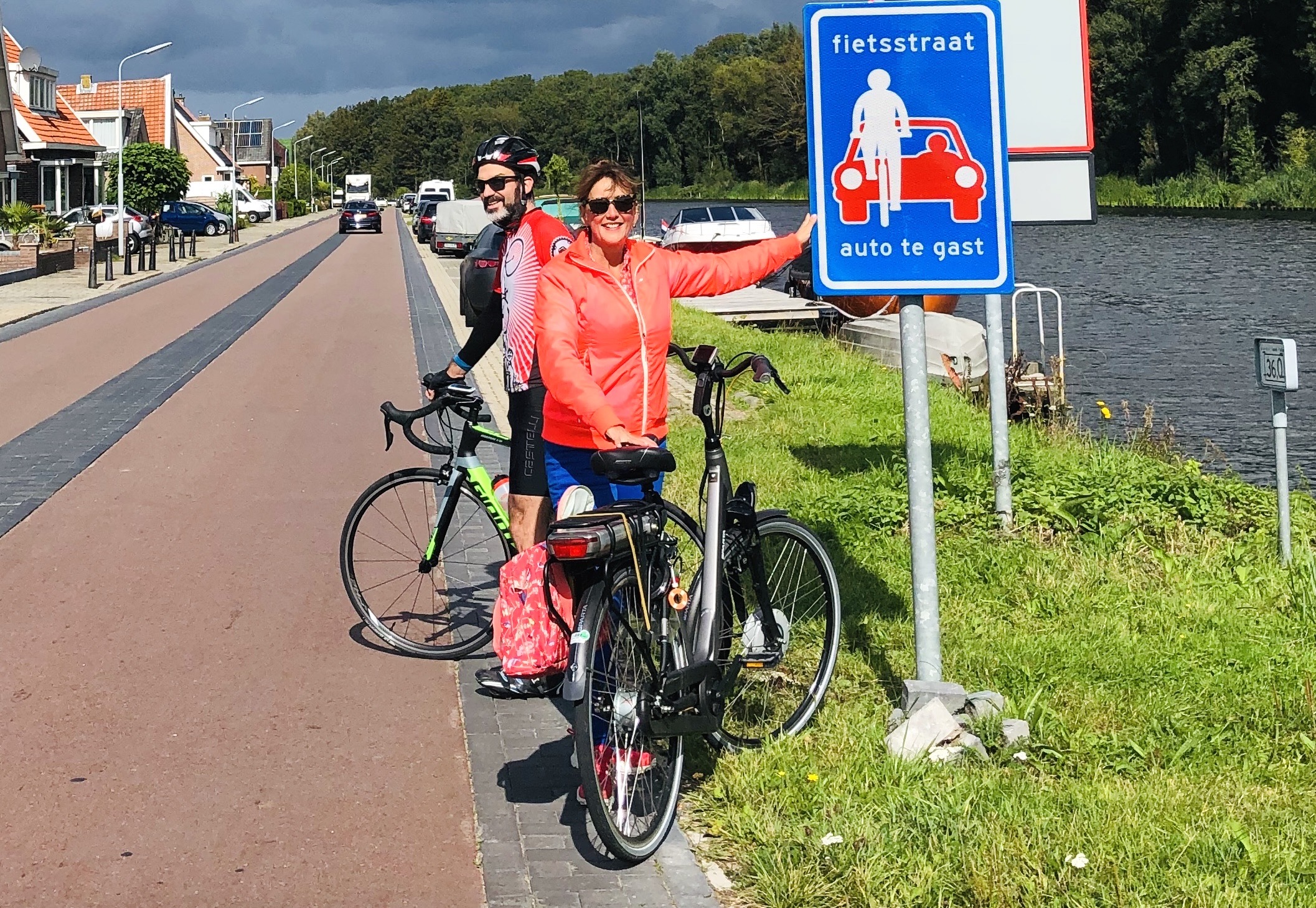 Marja Ruigrok wijst lachend naar een verkeersbord met de tekst "fietsstaat, auto te gast" terwijl ze naast haar fiets staat.