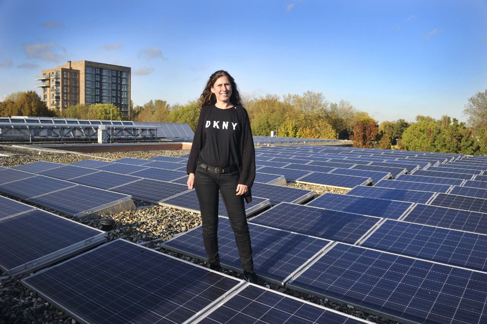 Mirjam Huisman staat op een dak met een groot aantal zonnepanelen onder een heldere blauwe lucht.