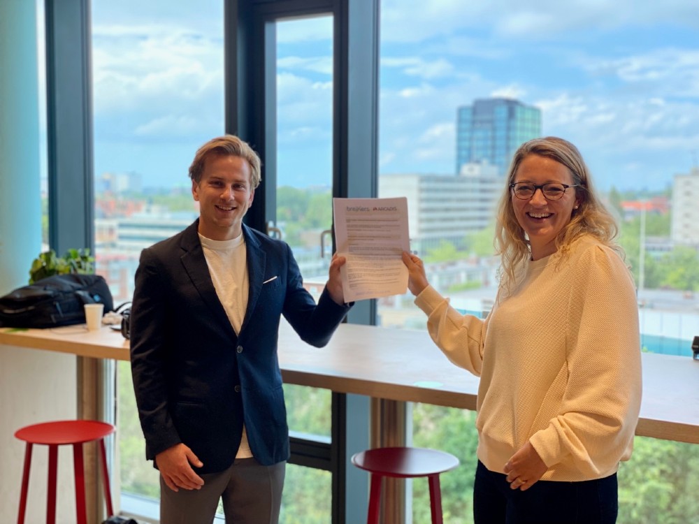 Twee mensen houden samen lachend de ondertekende samenwerkingsovereenkomst tussen Arcadis en Breikers omhoog.