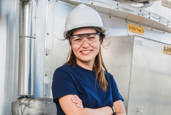 Vrouw met veiligheidshelm en bril glimlacht voor industriële installatie bij Bunge.