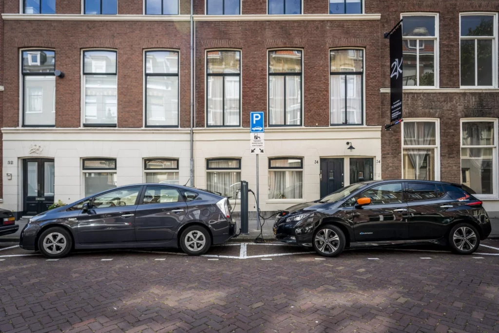 Twee elektrische auto’s zijn aangesloten op een laadpaal in een woonstraat.