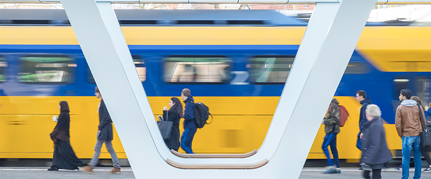 Reizigers lopen op een perron terwijl een gele en blauwe NS-trein voorbijrijdt.
